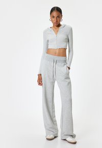 Grijze cropped zip-up hoodie met capuchon, gecombineerd met grijze wijde sweatpants. Zachte textuur, rafelrandjes en verstelbare tailleband met trekkoord.