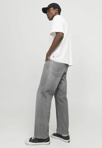 Jeans en denim gris associés à un t-shirt blanc et une casquette noire. Les jeans présentent une coupe classique et une poche arrière visible. Des sneakers noires complètent l'ensemble.