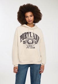 Felpa beige con cappuccio e tasca frontale, caratterizzata da una stampa grafica di un orso e testo: "Portland Stati Uniti Oregon 1986."