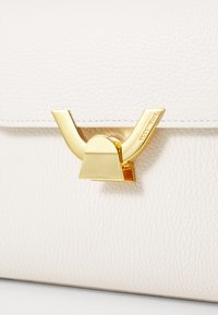 White textured leather handbag featuring a gold geometric clasp with angular detailing and a smooth finish.