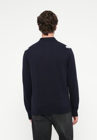 Marineblauer Strickpullover mit Kragen, der hellgraue Akzente an den Schultern sowie gerippte Bündchen und Saum hat. Weicher Stoff, lässige Passform.