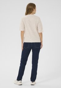 Svetlobežový svetr s krátkym rukávom a rebrovanými okrajmi, skombinovaný s tmavomodrými džínami. Oblečenie má ležérny strih s hladkou textúrou.