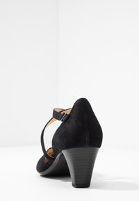 Scarpa nera in suede con tacco alto, punta affusolata, cinturino alla caviglia con fibbia e tacco conico texturizzato.