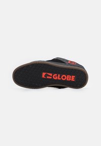 Suela de zapato de skate negra con un agarre texturizado. Presenta el logo rojo "GLOBE" y un contorno de goma marrón. Diseño minimalista, forma plana.