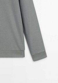 Szary długi rękaw z teksturowanej tkaniny. Posiada prążkowany mankiet i dół, prezentując gładki, bezszwowy fason bez wzorów.