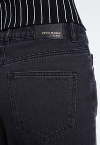Černé džíny z denimu s úzkým pasem, s označením "VERO MODA DENIM". Obsahují standardní zadní kapsy a nenápadné detaily šití.