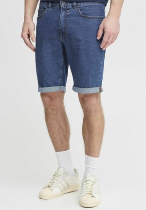 Denim shorts in dark blue, featuring rolled cuffs and five pockets. Worn with white socks and light-colored sneakers.
