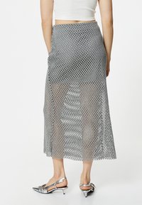 Mesh nederdel i sølv med et åbent diamantmønster, knælangt design og en tætsiddende talje. Matchet med metaliske spidse sko.