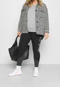 Svart och vit houndstooth skjortjacka, grå crewneck sweatshirt, svarta leggings med grå detaljer och vita sneakers. Svart handväska.