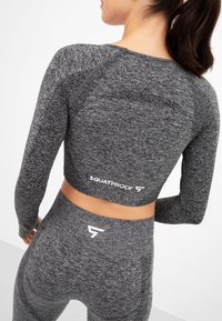 Gray athletic outfit featuring a cropped long-sleeve top and high-waisted leggings, made from textured fabric with "SQUATPROOF" branding.