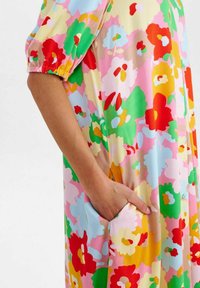 Blommönstrad klänning med livfulla färger som rosa, röd, gul och grön, med korta puffärmar och sidofickor. Slät tygtextur.