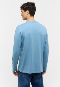 Long-sleeve shirt in light blue cotton, featuring a round neckline and a relaxed fit. Smooth texture, minimal detailing, and no visible graphics.