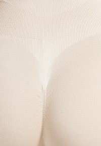 Nahaufnahme von beigem nahtlosem Rippstrickstoff, der den hohen Bund und den konturierten Körper eines Kleidungsstücks für eine glatte Passform formt.