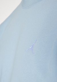 Hellblaues Sweatshirt mit hohem Kragen, weichem Material und kleinem lila gesticktem Jumpman-Logo auf der Brust.