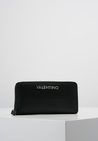 Portefeuille en cuir noir avec une finition texturée, doté d'une fermeture éclair et arborant le logo "VALENTINO" en lettres métalliques en relief sur le devant.