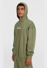 Grøn bomulds hoodie med kængurulomme og snøring i huen. Har teksten "The Future Surf Society" trykt på forsiden.