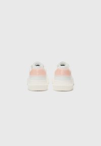Sneaker bianchi con finitura liscia, dotate di un accento rosa sul tallone, suola testurizzata e dettaglio del logo sulla parte posteriore.