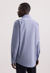 Camicia button-up azzurro chiaro in tessuto strutturato, con maniche lunghe e colletto a punta. Presenta bottoni ai polsini e un orlo dritto.