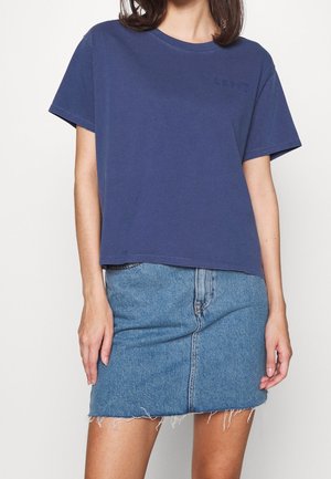 Kvinde iført en ensfarvet marineblå kortærmet t-shirt stoppet ned i en lyseblå denim miniskørt med frynset kant.