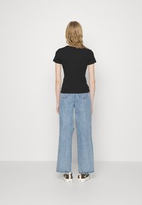 Svart tettsittende T-skjorte kombinert med høyhalsede lyseblå vide jeans, som viser et uformelt design og slitt kant. Sneakers med mønstrede detaljer.