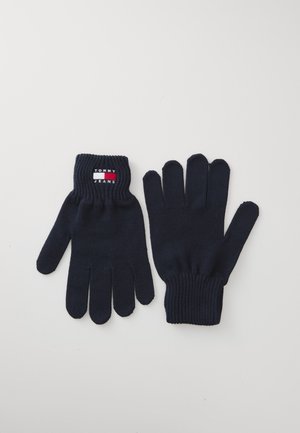 Par sorte strikkede handsker, den ene med mærkelogoet "Tommy Jeans" på manchet, lagt fladt på hvid baggrund.