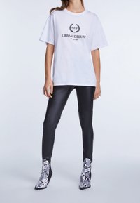 Vit bomull t-shirt med svart tryckt text, ihop med blanka svarta leggings och ankelstövlar i ormtryck i gråa och vita nyanser.