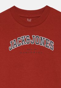Červená bavlnená mikina so štruktúrovaným okrúhlym výstrihom a veľkým logom "JACK&JONES" v bielej a čiernej farbe, s nápisom "EST. 90 WORLDWIDE" pod ním.