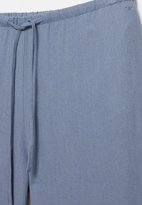 Pantalon en lin bleu clair avec taille élastique et cordon cousu, avec un logo brodé discret près de la taille.