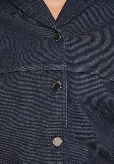 Dark blue denim jacket with metal snap buttons and visible topstitching, showing the upper chest and collar area.