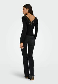 Zwarte longsleeve top met een V-halslijn en kantafwerking, gecombineerd met zwarte flared jeans en hakschoenen. Eenvoudig ontwerp.