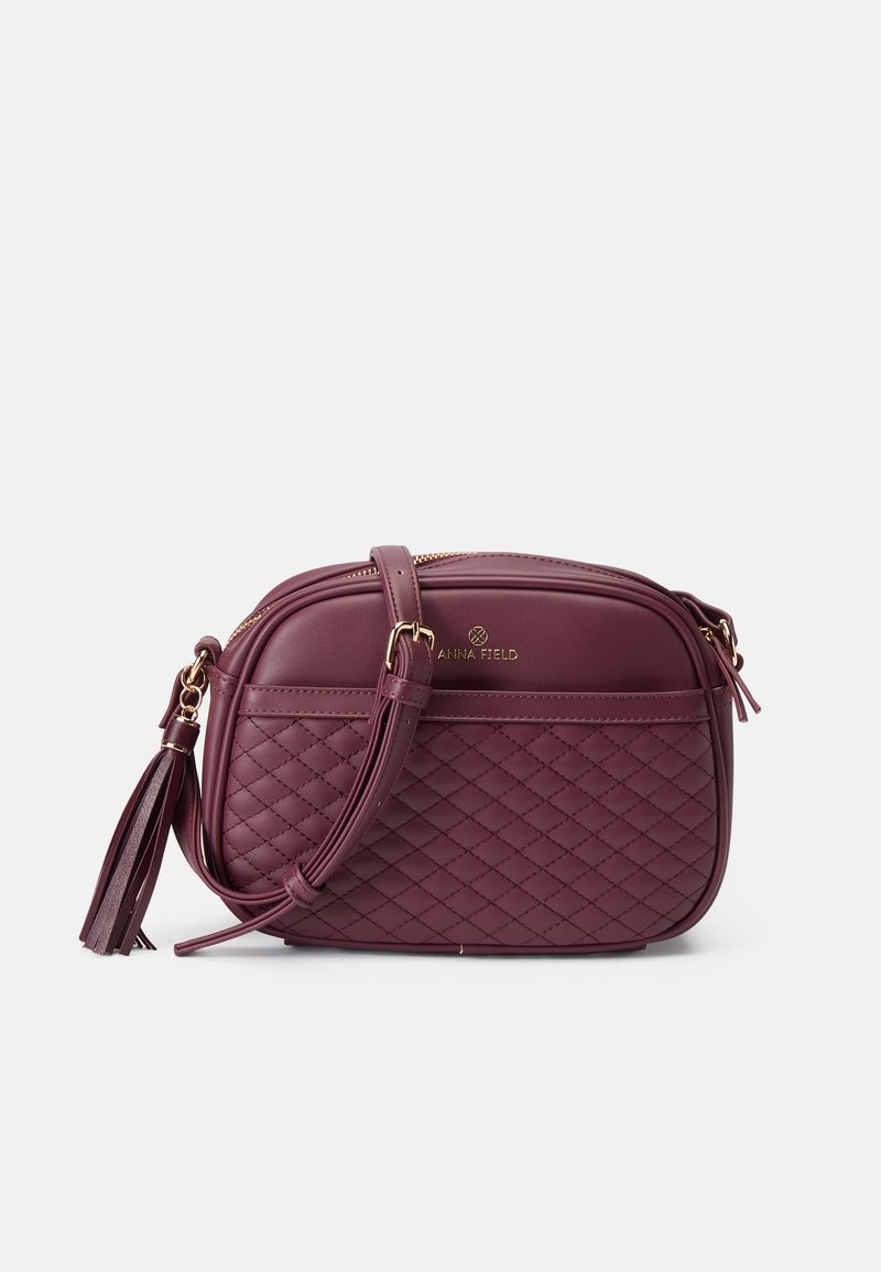 Burgundyröd crossbody-väska i syntetläder, med en kviltad mönstring, guldfärgade detaljer och en avtagbar tofs.