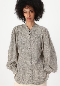 Lys beige skjorte med svart spraglet mønster, med knappelukking foran og puffer lange ermer. Mykt, teksturert stoff.
