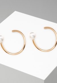 Goldene Creolen mit einem glatten Perlenakzent. Das Design ist offen und kreisförmig, mit einer polierten Oberfläche.
