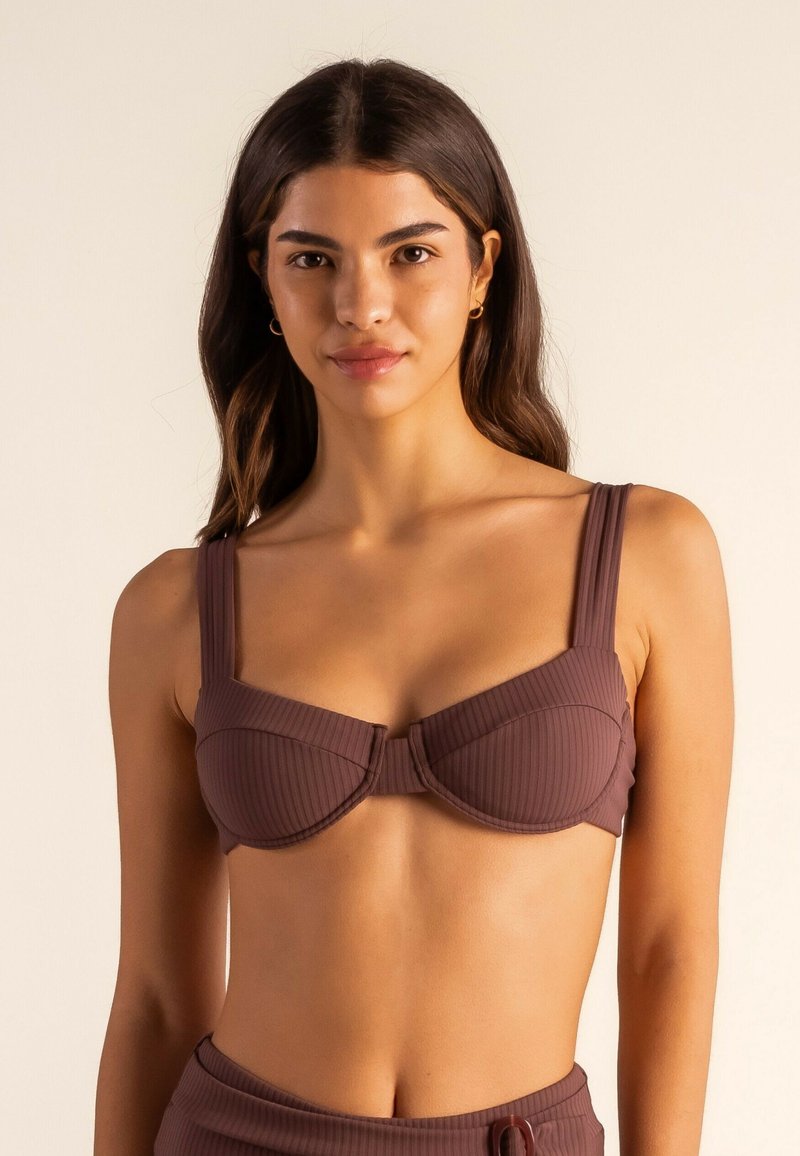 Top de bikini marrón con relieve, con tirantes anchos, diseño con aros y detalle de lazo en el frente. Textura suave y estilo ajustado.