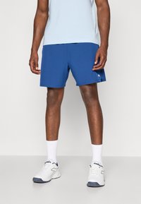 Blå sportsshorts, letvægtsstof, elastisk talje, sidelommer, stylet med hvide sneakers og ankel-lange sokker.