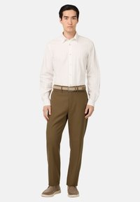 Camicia bianca a maniche lunghe con righe verticali, abbinata a pantaloni marroni e una cintura intrecciata marrone. Scarpe casual marroni completano l'outfit.