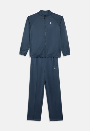 Tumesinine kaheosaline dressikomplekt, millel on lukuga jakk ja elastsed mansetid, kus rinnal ja reiel on väikesed valged Jumpman logod.