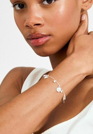 Hõbedast käevõru, millel on lillemotiiv, väikesed pärlid ja peenike kett. Mudeli nahk on sile ja üleval valge soonikkoes topp.