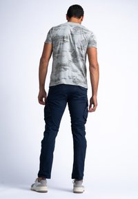 Lichtgrijze t-shirt met een gestructureerd, abstract patroon. Marineblauwe cargobroek met zijzakken. Casual schoenen in wit en grijstinten.