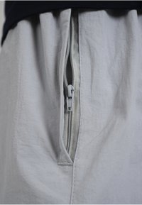 Gros plan d'une fermeture éclair argentée partiellement ouverte sur un tissu gris clair avec une ceinture noire au-dessus.