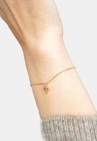 Bracciale in oro con un piccolo ciondolo a forma di foglia, caratterizzato da maglie sottili e una finitura lucida, indossato su un polso con texture cutanea visibile.