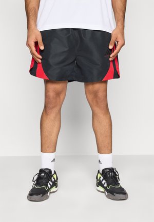 Pantaloni scurți atletici negri cu panouri laterale roșii, făcuți din material ușor. Asortați cu adidași negri și verzi și șosete albe.
