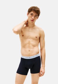 Boxer shorts de algodón negros con una cinta elástica azul claro que presenta el logo de "TOMMY HILFIGER", con textura suave y diseño ajustado.