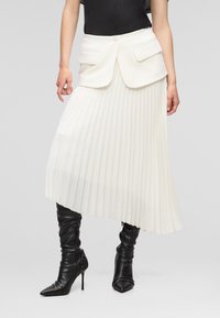 White pleated skirt with fitted bodice and two front pockets, paired with high black leather stiletto boots featuring pointed toes.