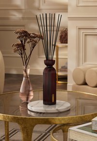 Rød ribbet glassdiffuser med svarte pinner, plassert på en rund hvit marmorbase. Medikamentert med en rosa stripete vase og tørkede blomster.