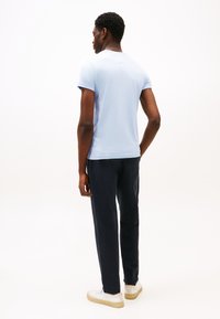 Šviesiai mėlynas trumpomis rankovėmis marškinėlis iš minkštos medžiagos, derinamas su tamsiai mėlynomis kelnėmis ir baltais sportbačiais su smėlio spalvos padais. Minimalistinis dizainas, be raštų.