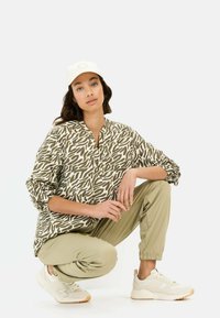 Lichte, lange mouw blouse met een abstract patroon in bruin en beige, gecombineerd met slim-fit kaki broeken en crèmekleurige sneakers.
