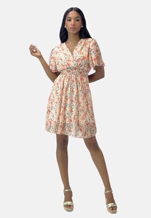 Blomstret kjole i pastel fersken, med V-udskæring, puffærmer og smocked talje. Båret med gyldne strop sandaler.