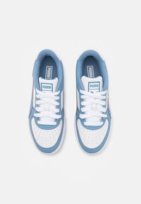 Un par de zapatillas Puma blancas y azules con cordones blancos, cajas de dedos perforadas y interiores acolchados azules, mostradas desde arriba sobre un fondo blanco.