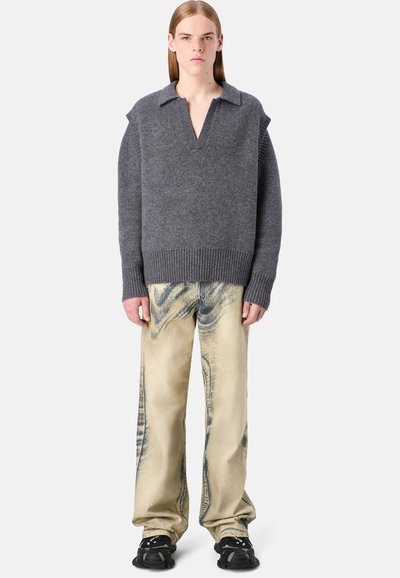 Grauer Strickpullover mit kragenförmigem Ausschnitt, kombiniert mit beigefarbenen Hosen mit marmorierter Struktur und schwarzem Schuhwerk mit Riemen.